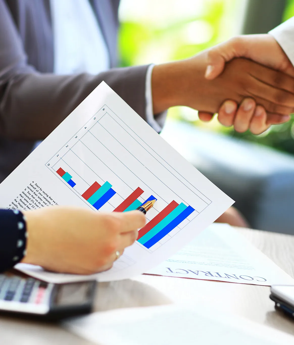 A handshake over a reviewed contract and performance charts